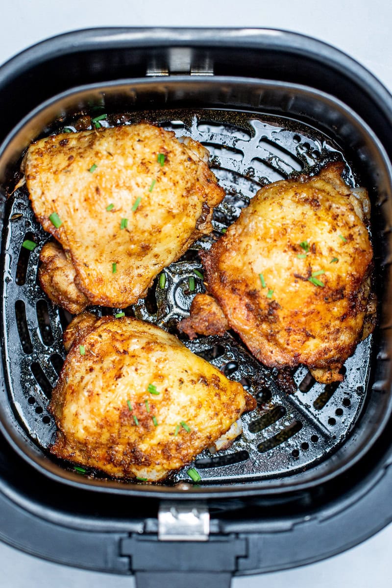 Chicken thighs in an air fryer basket with chopped chives on top of crispy skin.