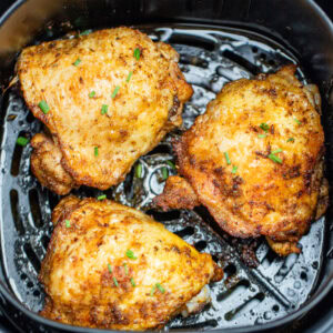 Chicken thighs in an air fryer basket with chopped chives on top of crispy skin.