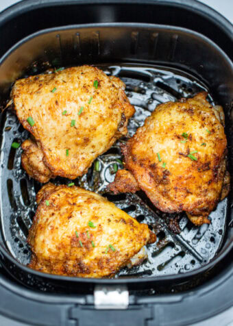 Chicken thighs in an air fryer basket with chopped chives on top of crispy skin.