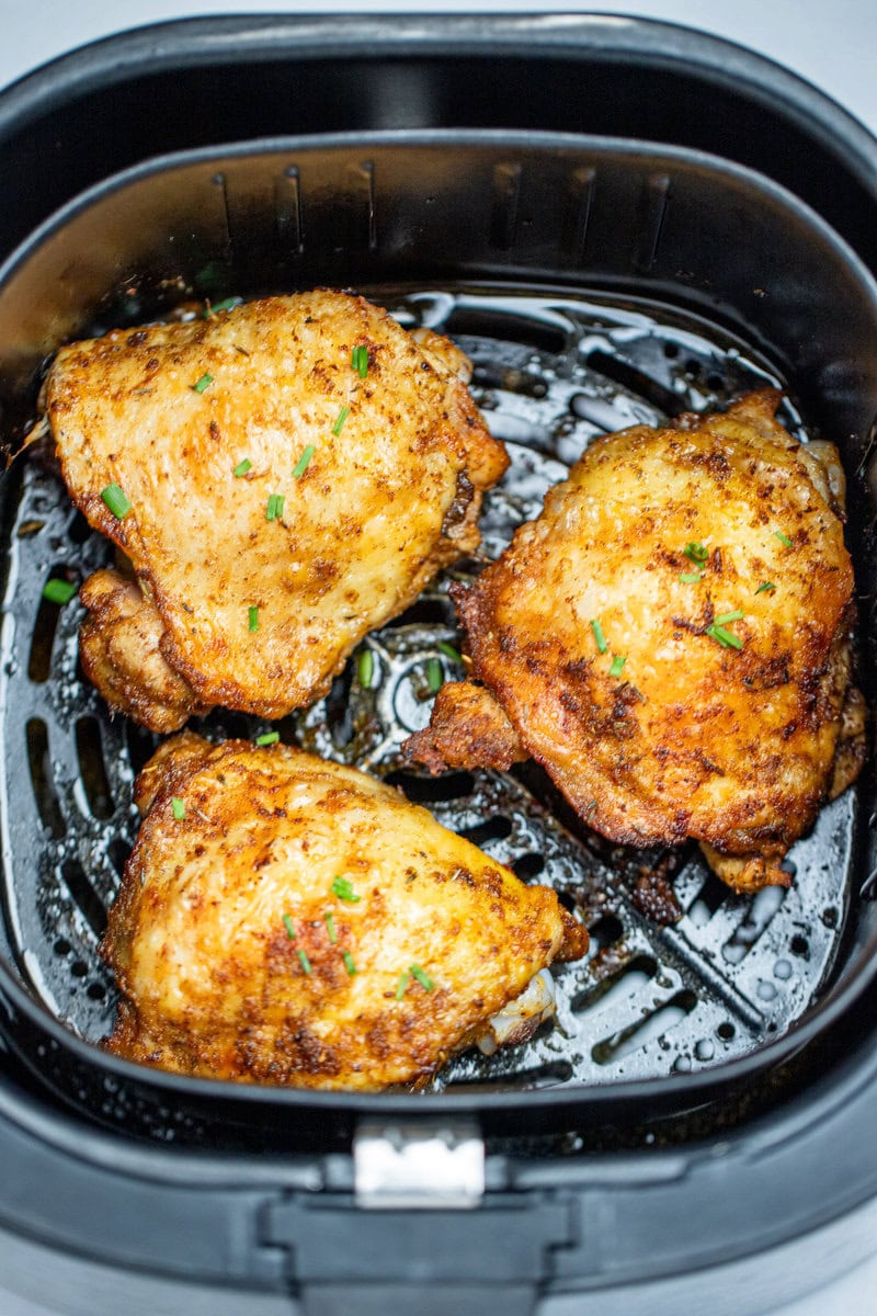 Chicken thighs in an air fryer basket with chopped chives on top of crispy skin.