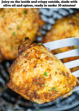 Pinterest pin with chicken thighs in an air fryer basket with chopped chives on top of crispy skin, with a spatula lifting one up.