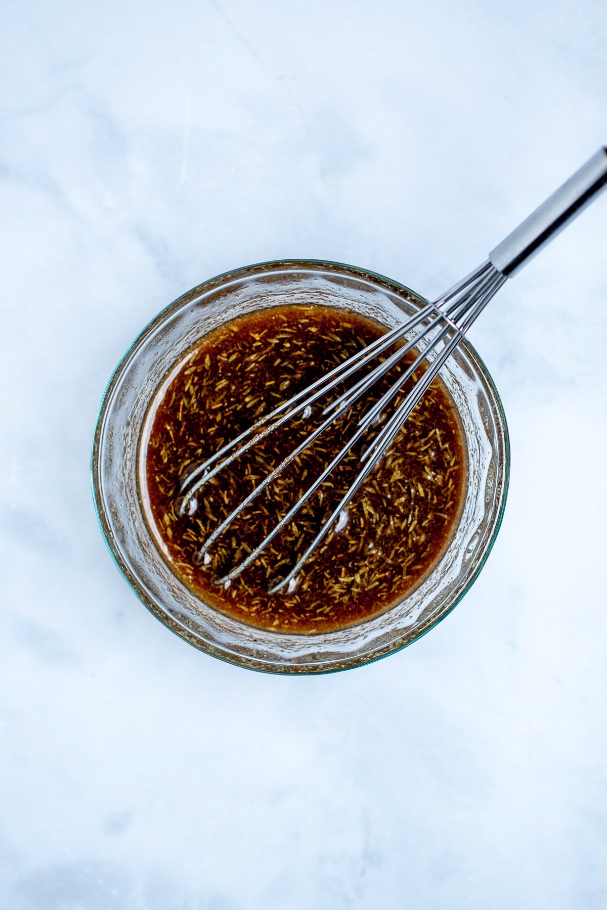 A small glass bowl with the maple glaze ingredients and a whisk in the bowl.