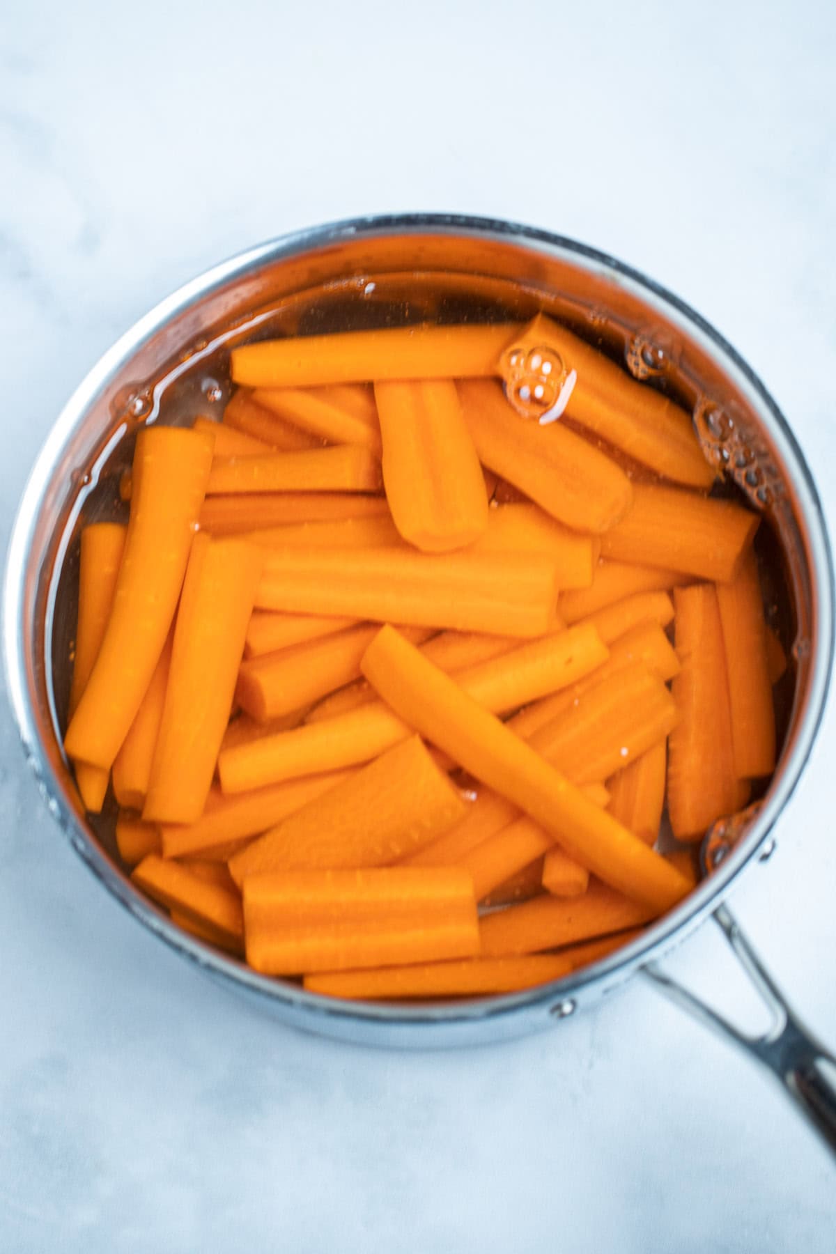 A saucepan with raw carrots and water covering the carrots.