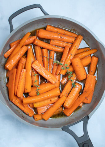 A skillet with cooked maple glazed carrots with fresh thyme sprigs on top, resting on a table.