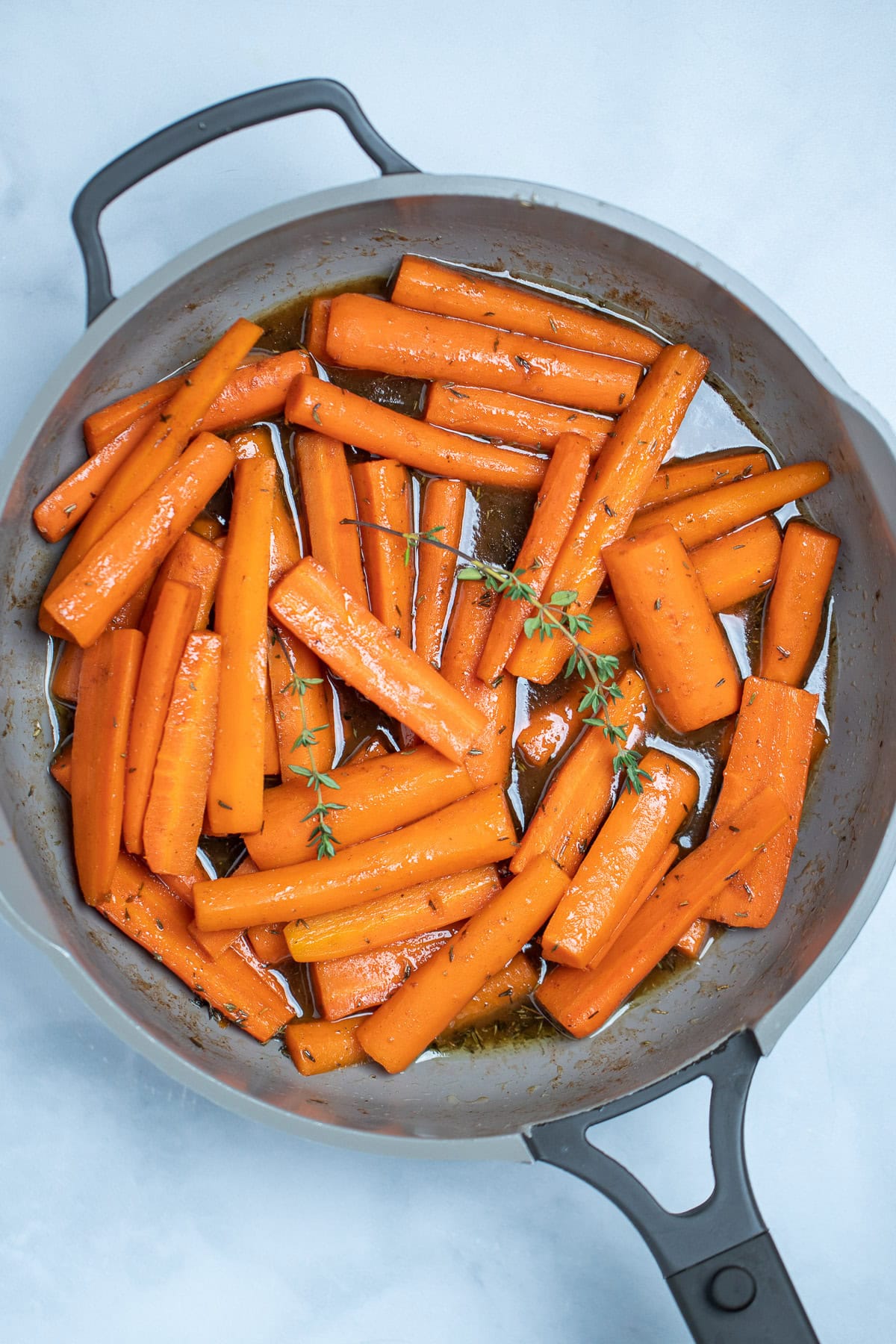 A skillet with cooked maple glazed carrots with fresh thyme sprigs on top, resting on a table.