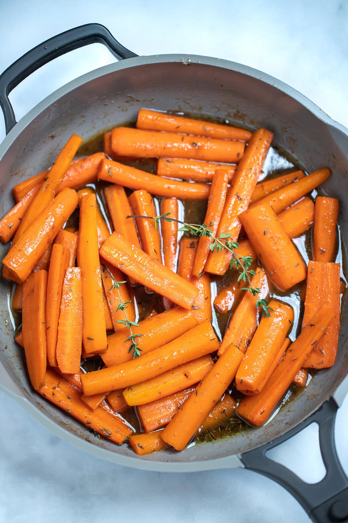 A skillet with cooked maple glazed carrots with fresh thyme sprigs on top, resting on a table.