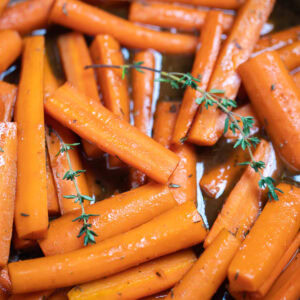 A closeup in a skillet with cooked maple glazed carrots with fresh thyme sprigs on top.