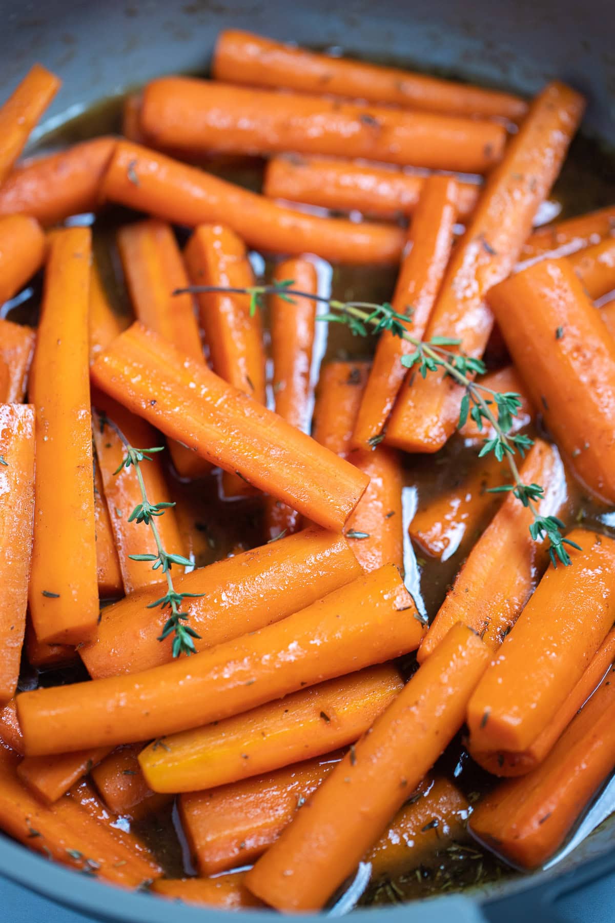 A closeup in a skillet with cooked maple glazed carrots with fresh thyme sprigs on top.