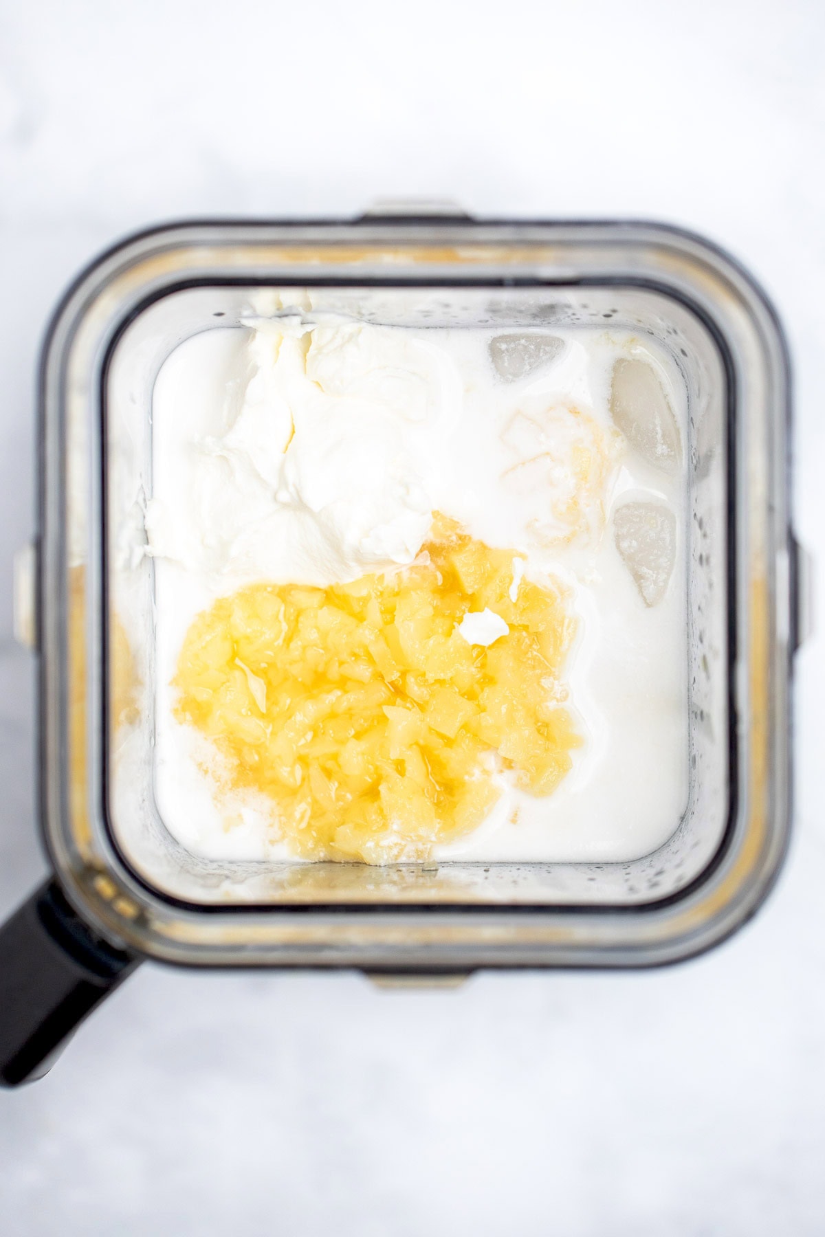 A blender with coconut milk, pineapple, banana, and greek yogurt before blending.