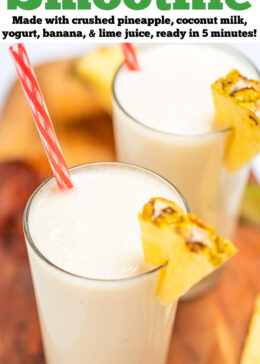 Pinterest pin with a tall glass with a pineapple wedge garnish and a straw, full of pina colada smoothie, with another glass behind it, on a cutting board with pineapple and lime wedges.