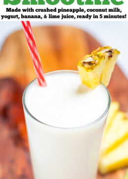 Pinterest pin with a tall glass with a pineapple wedge garnish and a straw, full of pina colada smoothie, with another glass behind it, on a cutting board with pineapple and lime wedges.