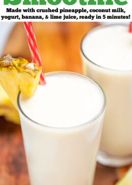 Pinterest pin with a tall glass with a pineapple wedge garnish and a straw, full of pina colada smoothie, with another glass behind it, on a cutting board with pineapple and lime wedges.