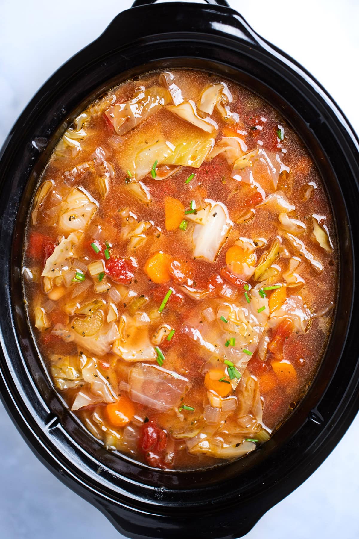 A slow cooker with cabbage soup fully cooked and topped with chives before being served.