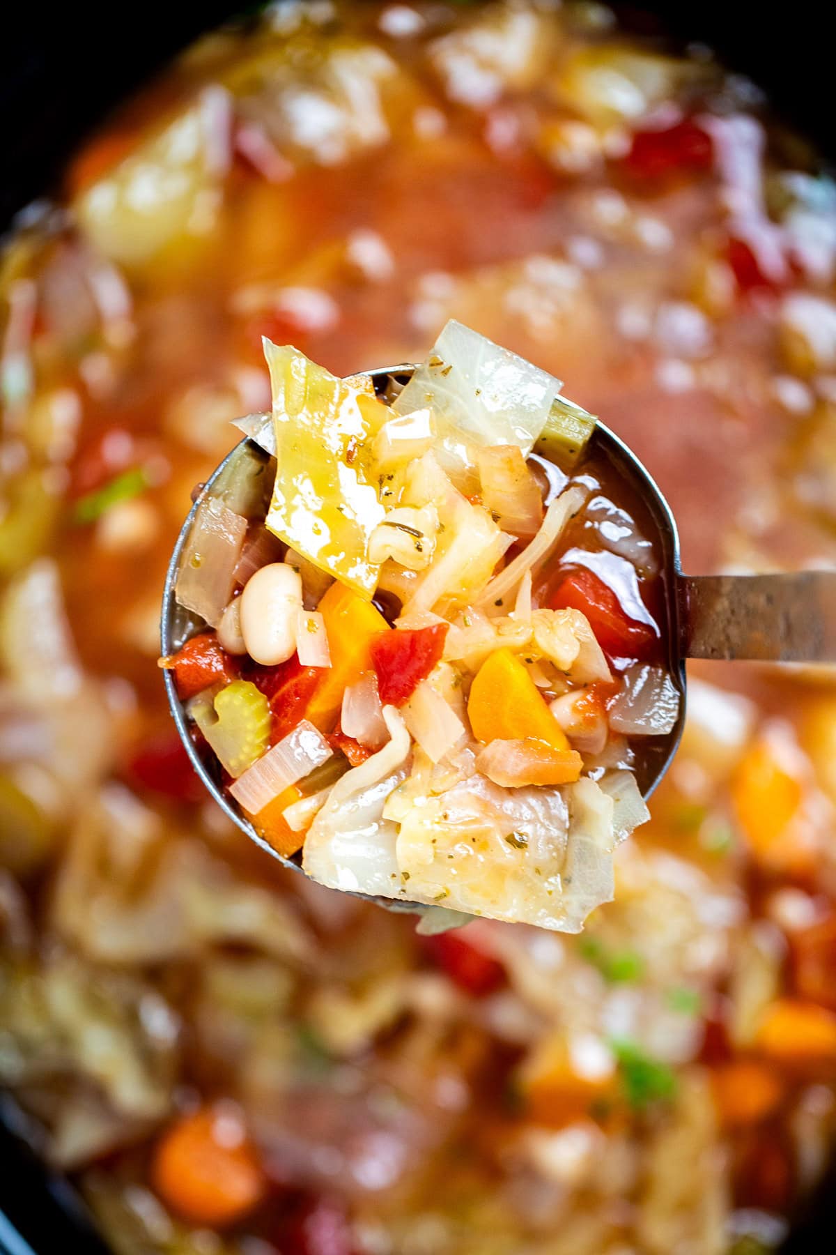 A ladle lifting up a serving of slow cooker cabbage soup from the crockpot.