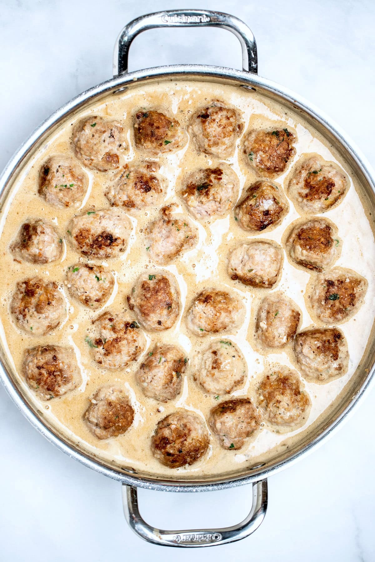 A large skillet with browned meatballs simmering in gravy.