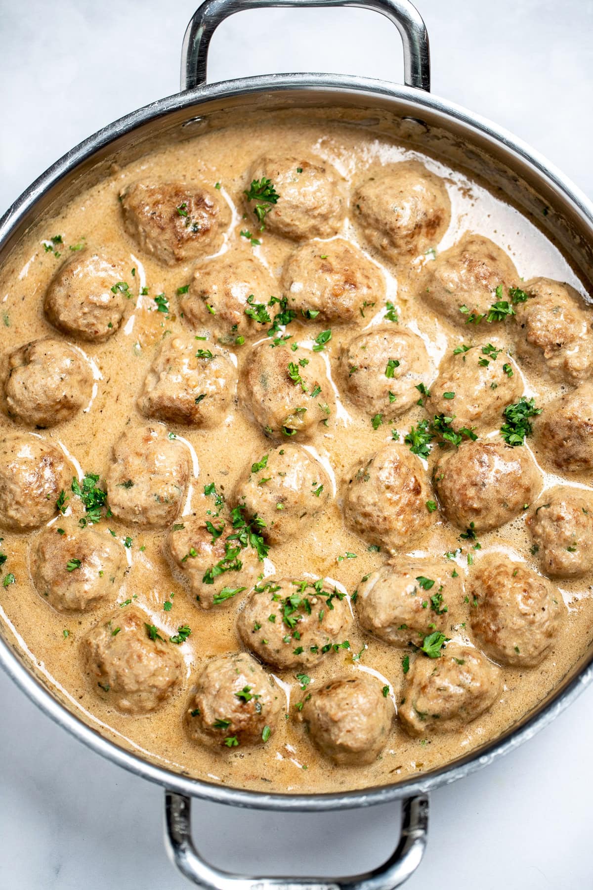 A large skillet full of meatballs in gravy topped with fresh parsley.