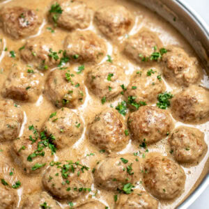 A large skillet full of meatballs in gravy topped with fresh parsley.