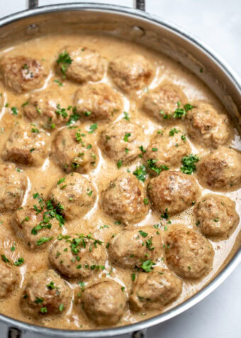 A large skillet full of meatballs in gravy topped with fresh parsley.