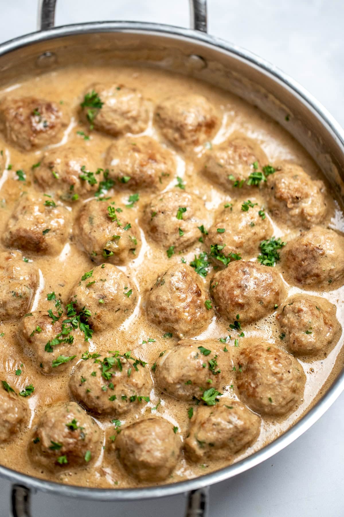 A large skillet full of meatballs in gravy topped with fresh parsley.