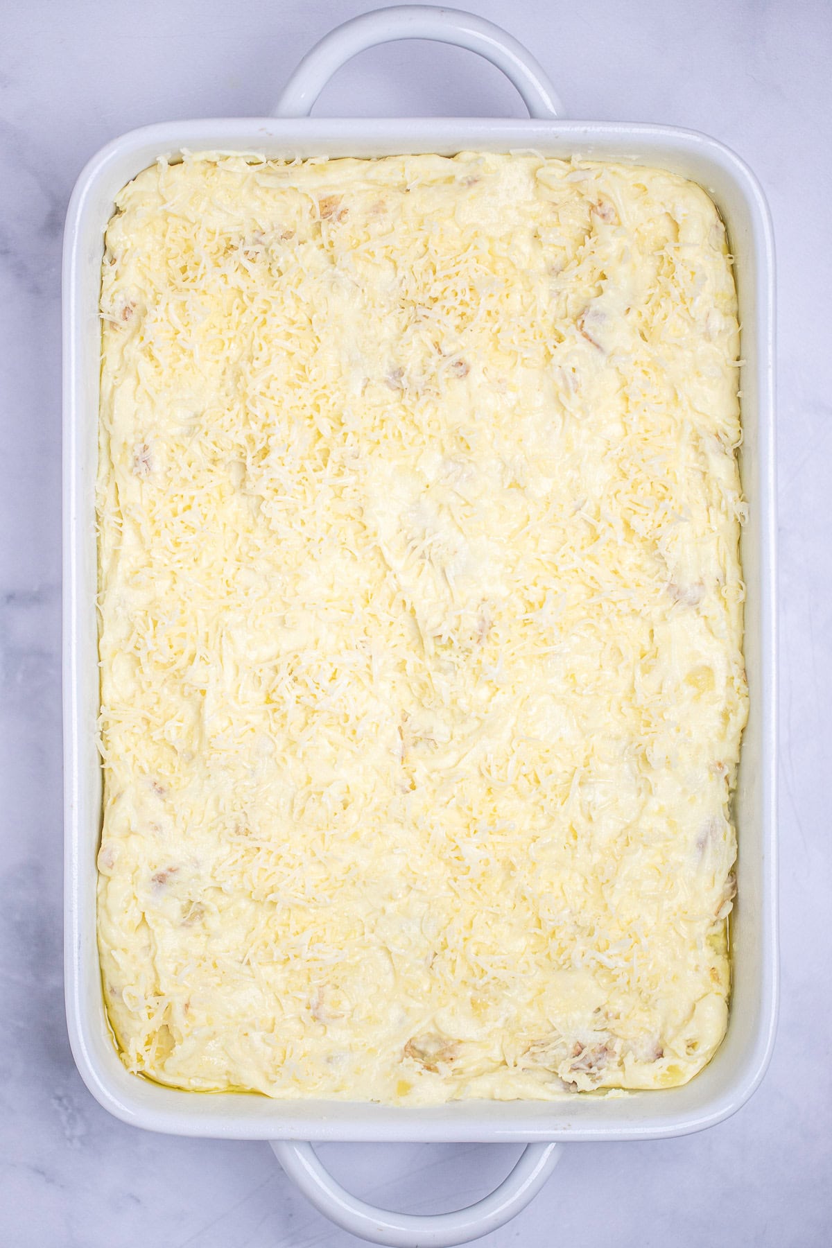 A casserole dish full of mashed potatoes topped with muenster cheese before being baked.