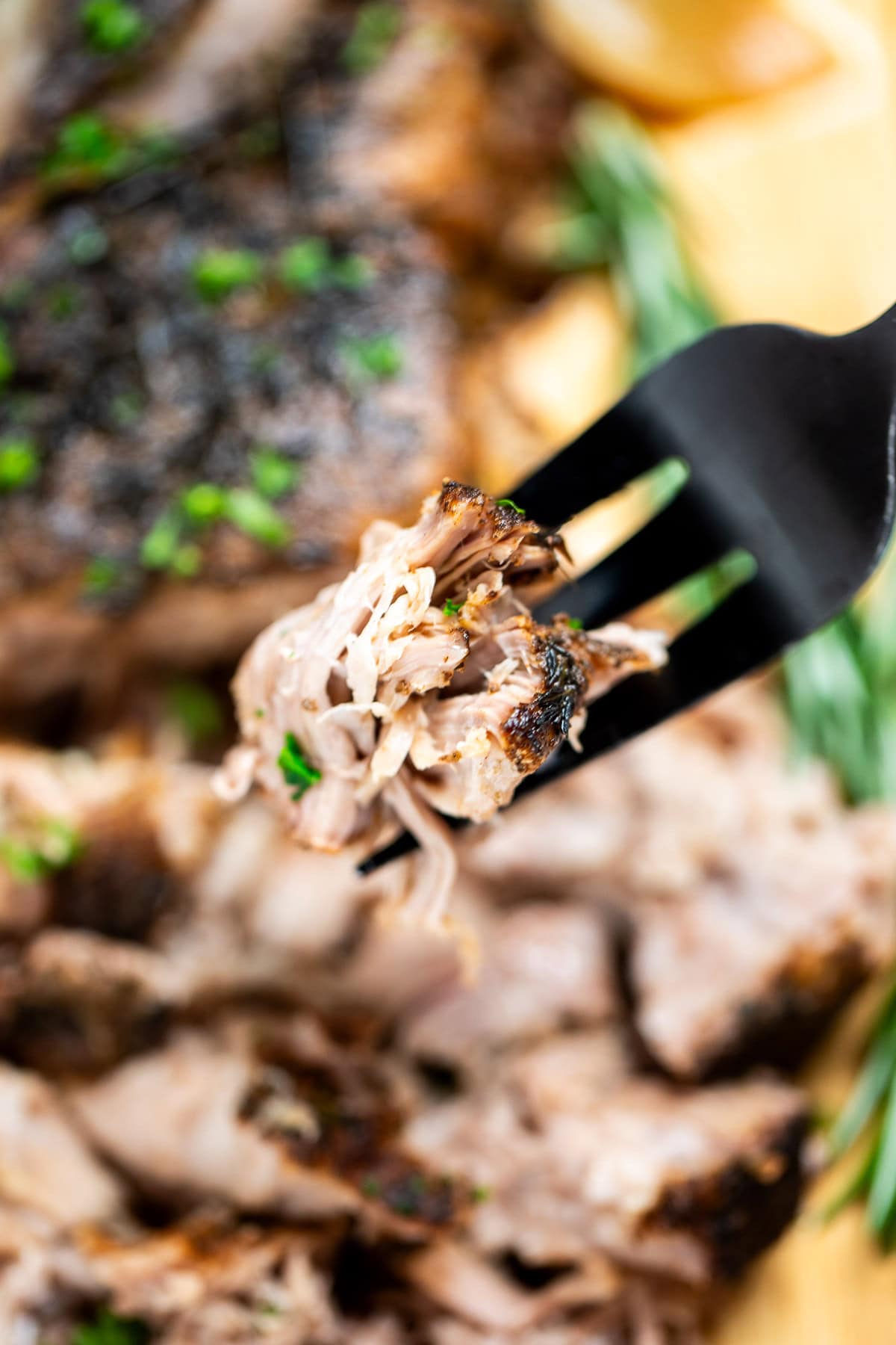 A fork holding up a piece of pork roast, with a slow cooker pork roast in the background on a cutting board.