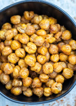 A bowl on a table with crispy air fryer chickpeas coated in seasoning.