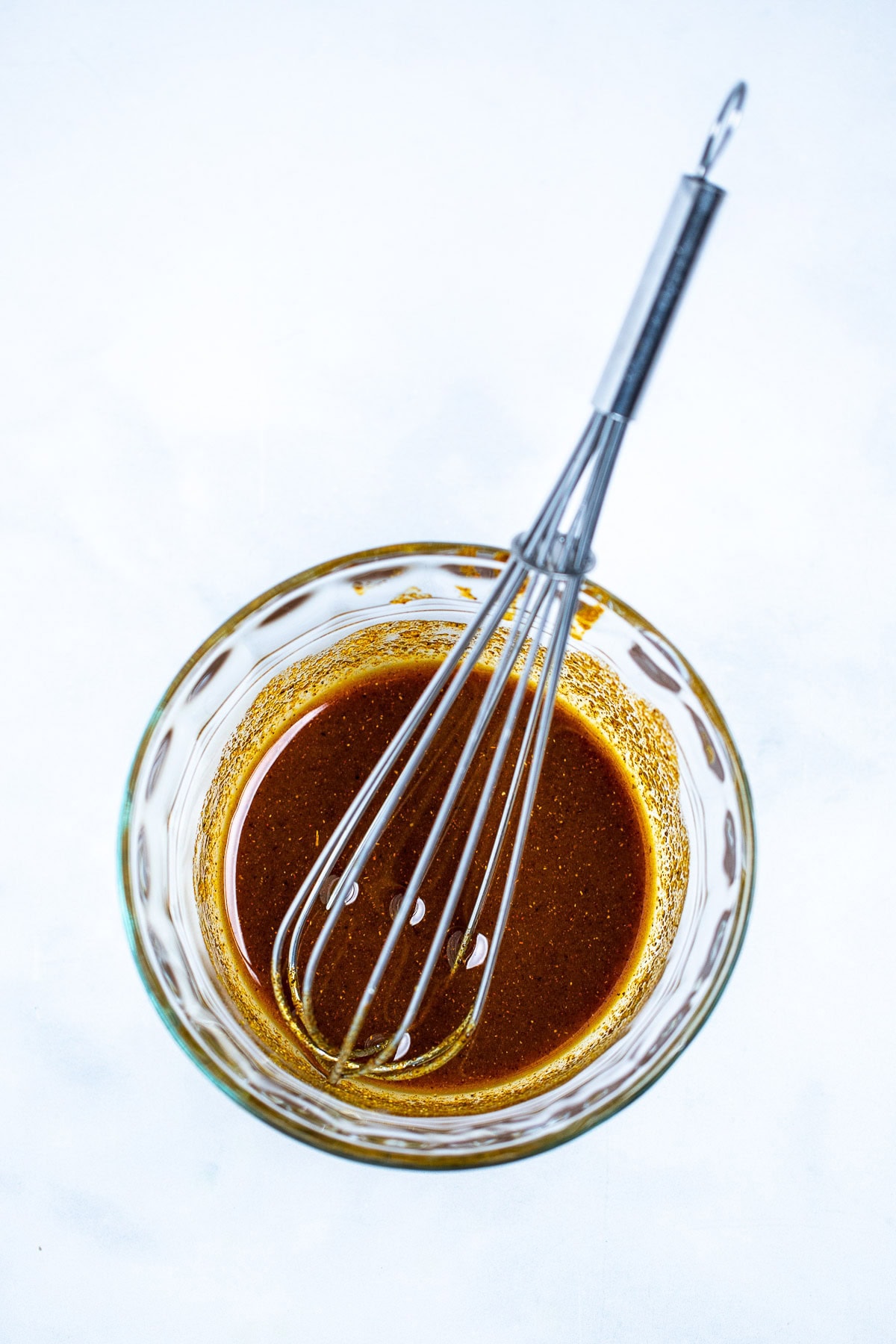 A small glass bowl with olive oil and seasoning mixed together with the whisk in the bowl.