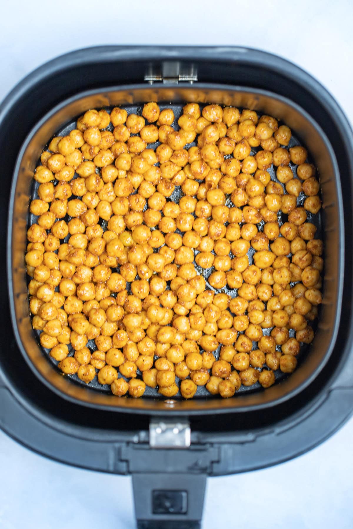 An air fryer basket with chickpeas coated in olive oil and seasoning before being air fried.