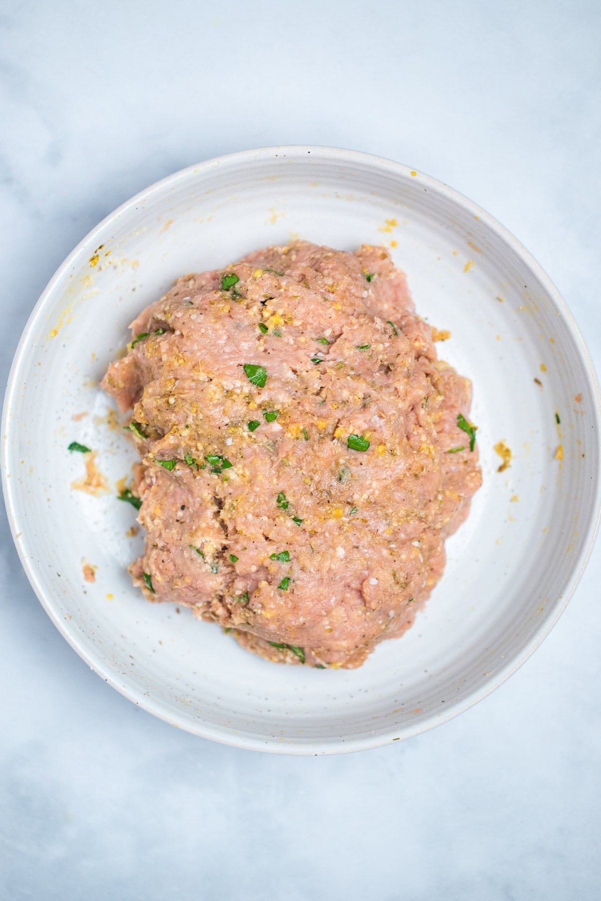 Ground turkey mixed with all other ingredients in a bowl on the table.