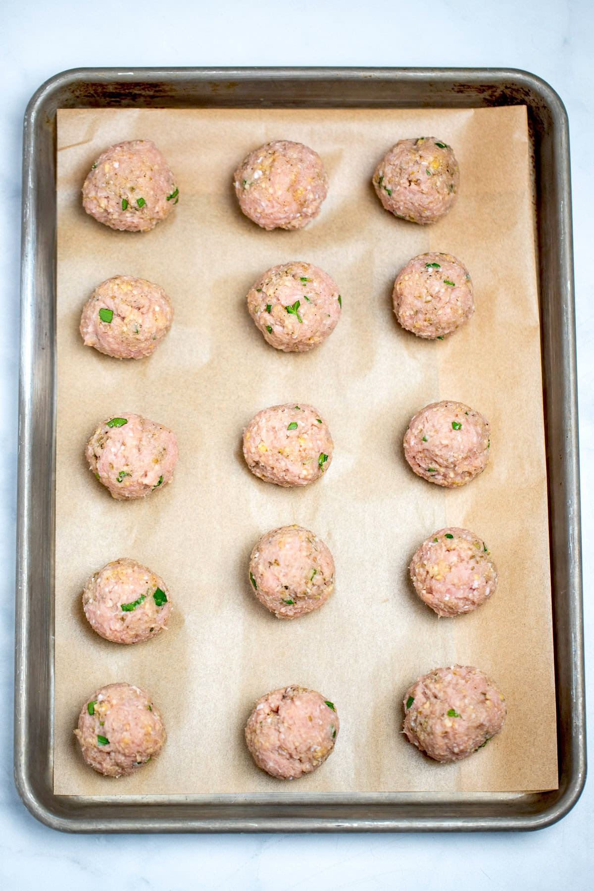 A sheet pan lined with parchment paper, with raw meatballs in rows of 3 on the sheet pan.