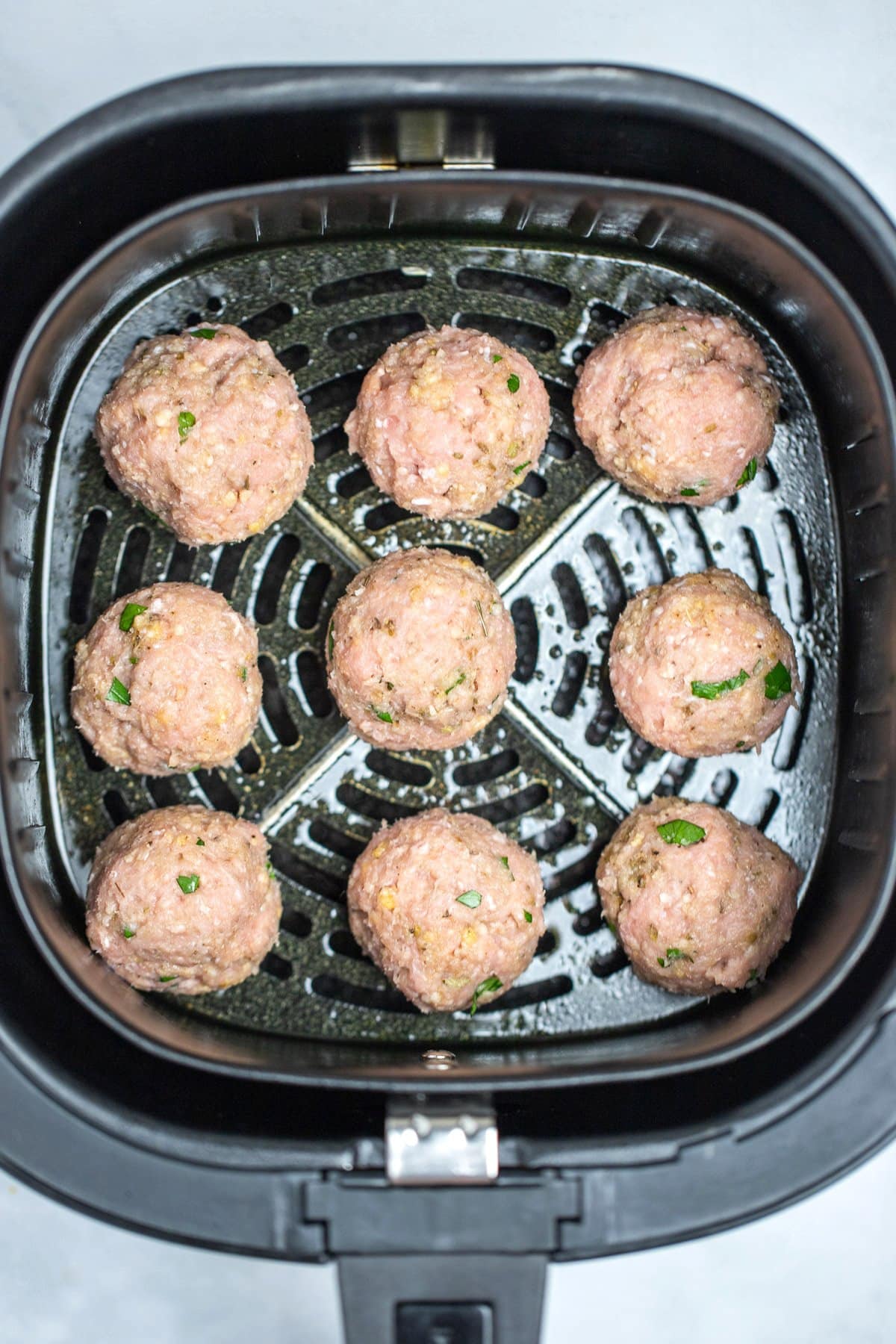 An air fryer basket with raw meatballs before being cooked.