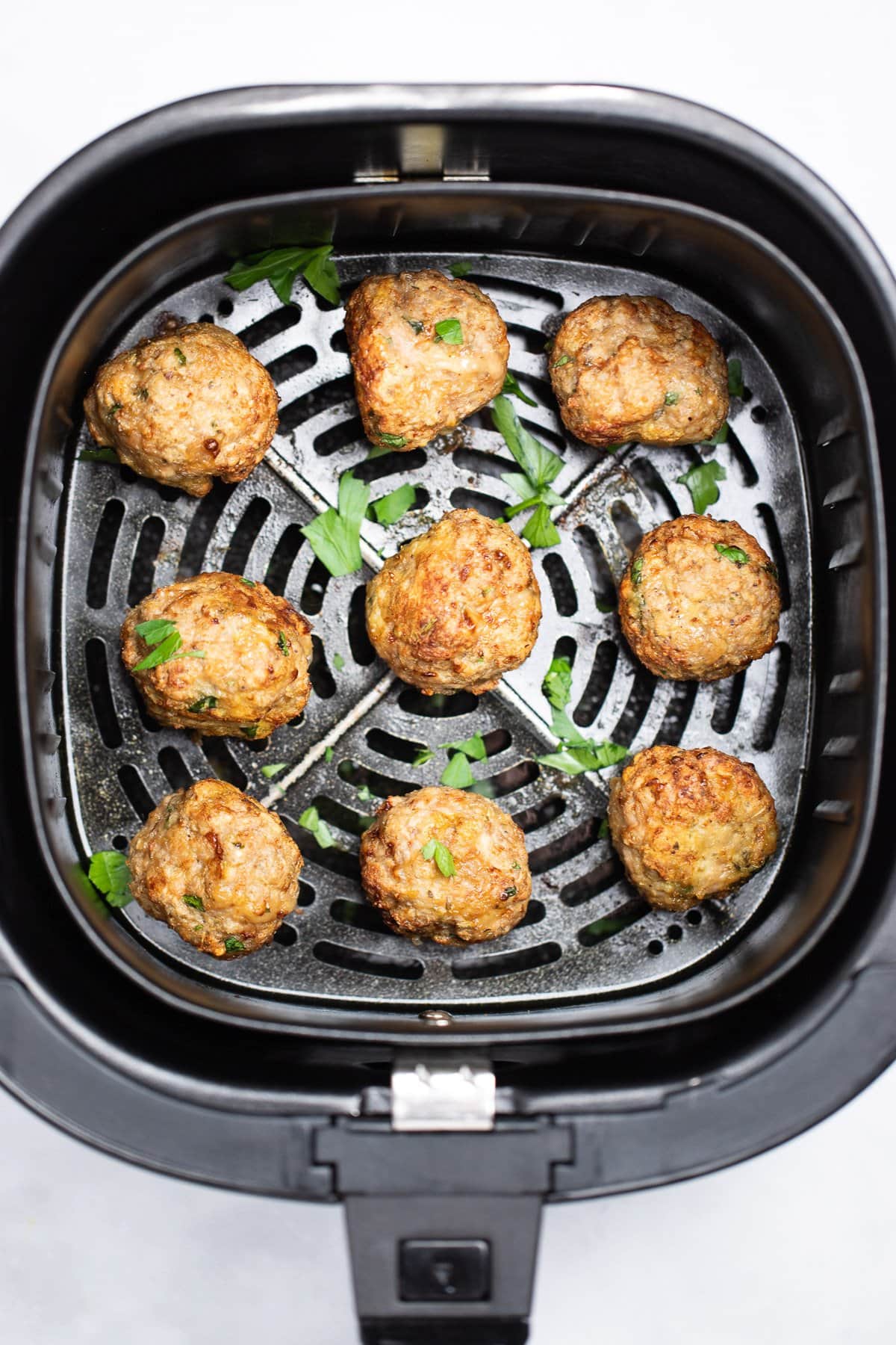 Air fryer turkey meatballs in an air fryer basket after being cooked. They're brown and caramelized and topped with fresh parsley.