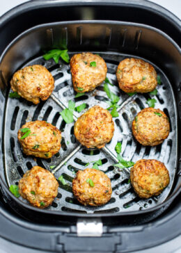 Air fryer turkey meatballs in an air fryer basket after being cooked. They're brown and caramelized and topped with fresh parsley.