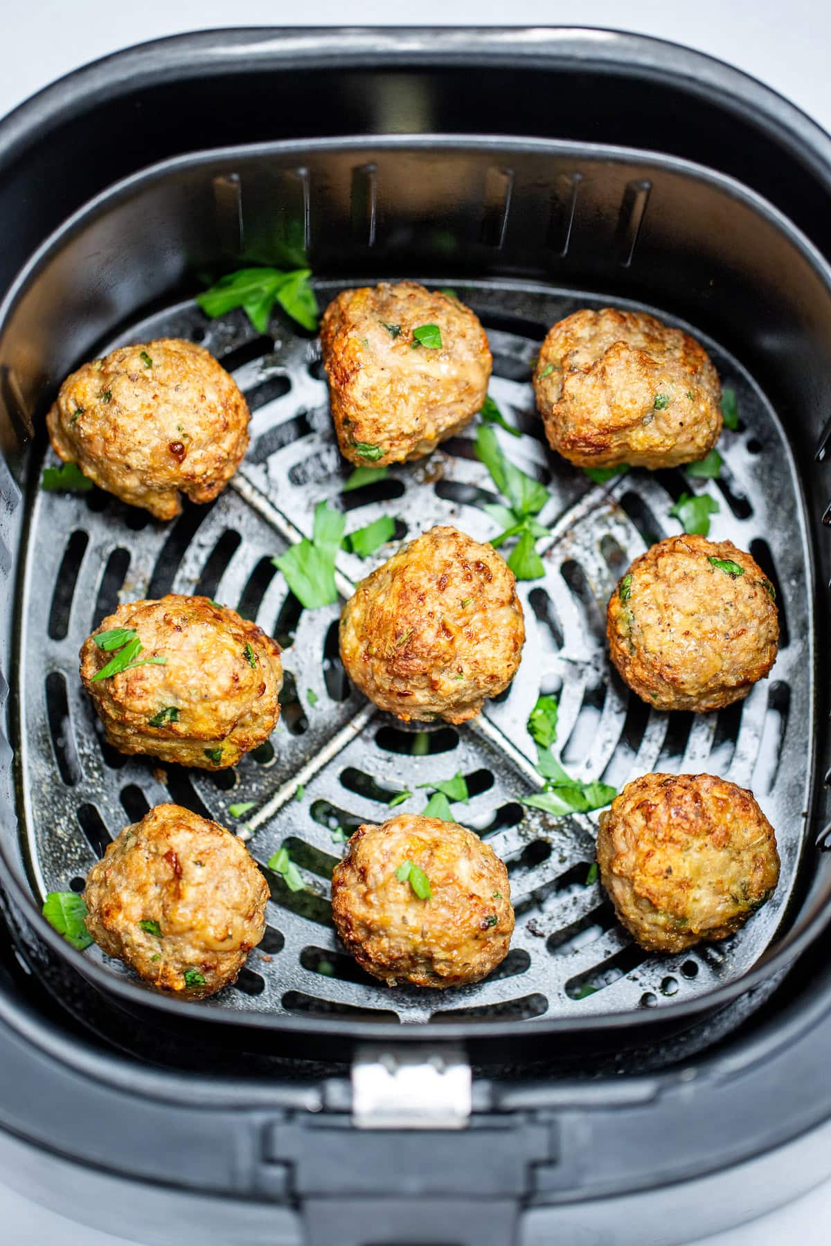 Air fryer turkey meatballs in an air fryer basket after being cooked. They're brown and caramelized and topped with fresh parsley.