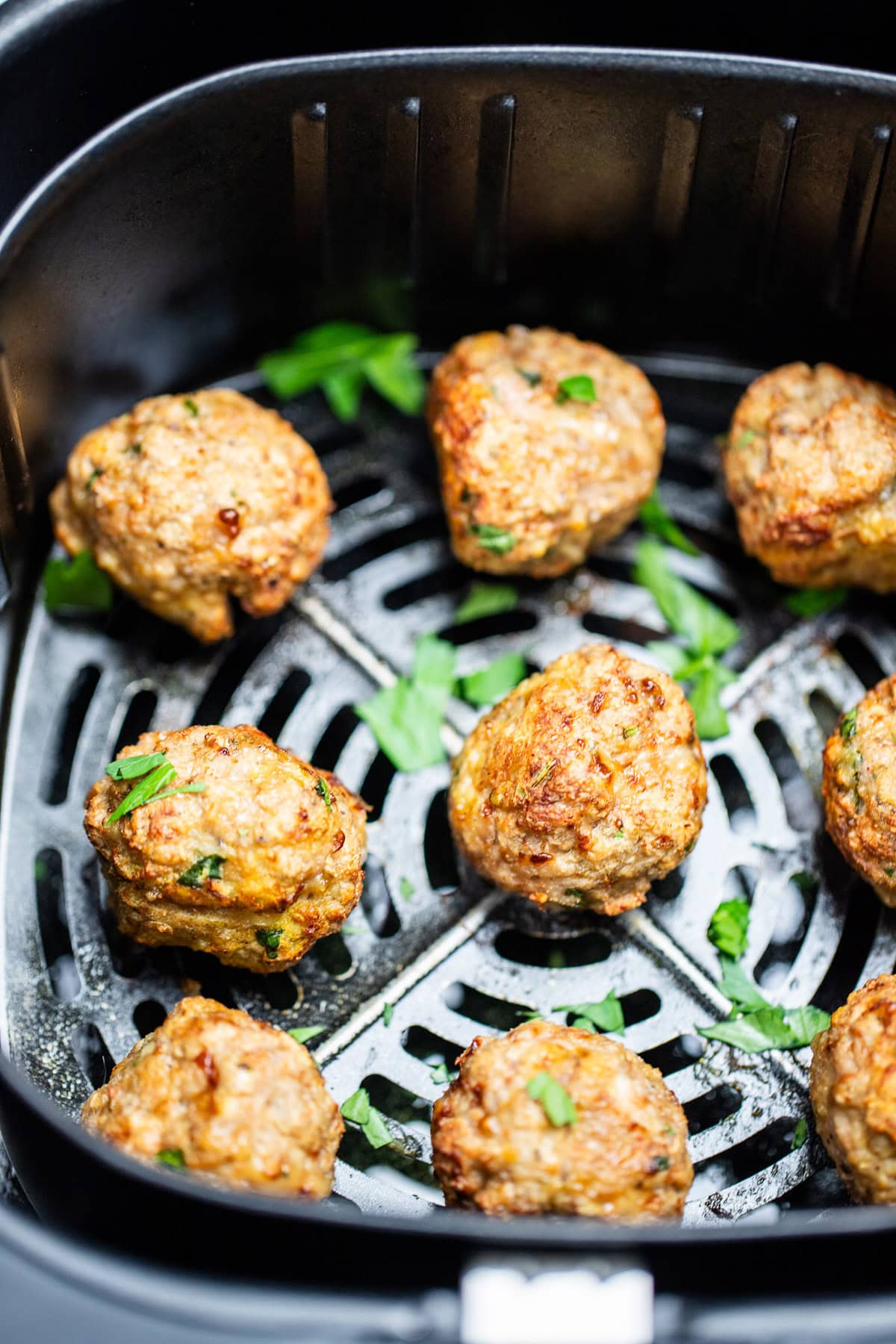 Air fryer turkey meatballs in an air fryer basket after being cooked. They're brown and caramelized and topped with fresh parsley.