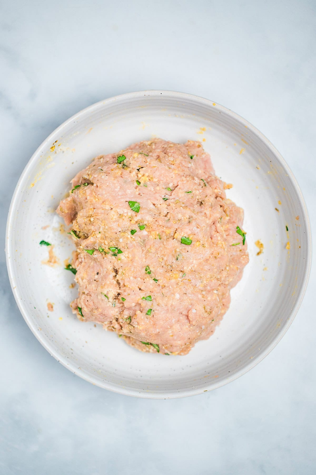 All of the ingredients for turkey meatballs mixed together in a bowl on the table.