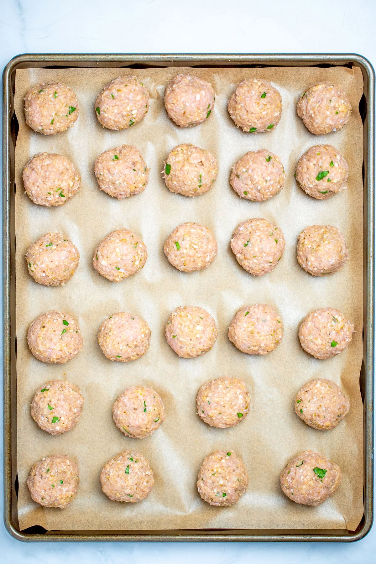 Raw turkey meatballs on a sheet pan lined with parchment paper before being baked.