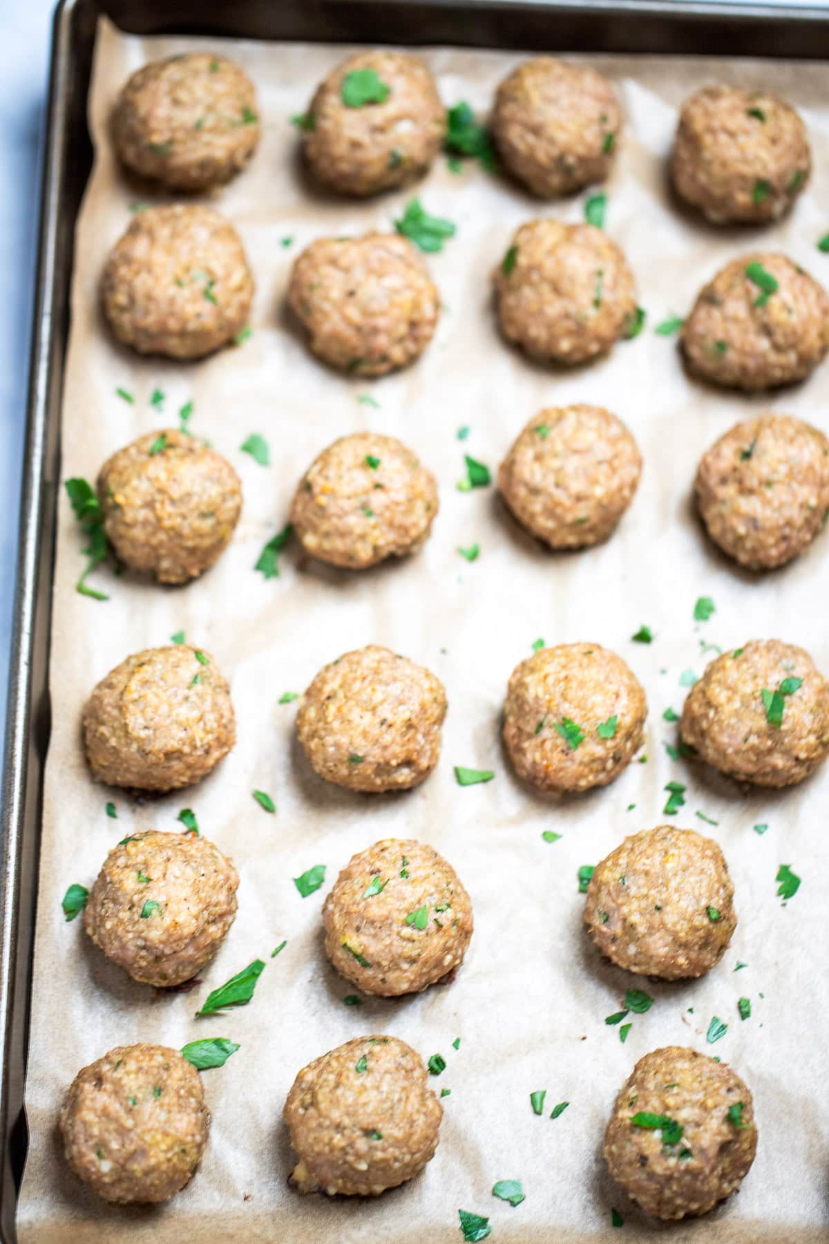 Baked turkey meatballs on a sheet pan lined with parchment paper, fully cooked and topped with fresh chopped parsley.