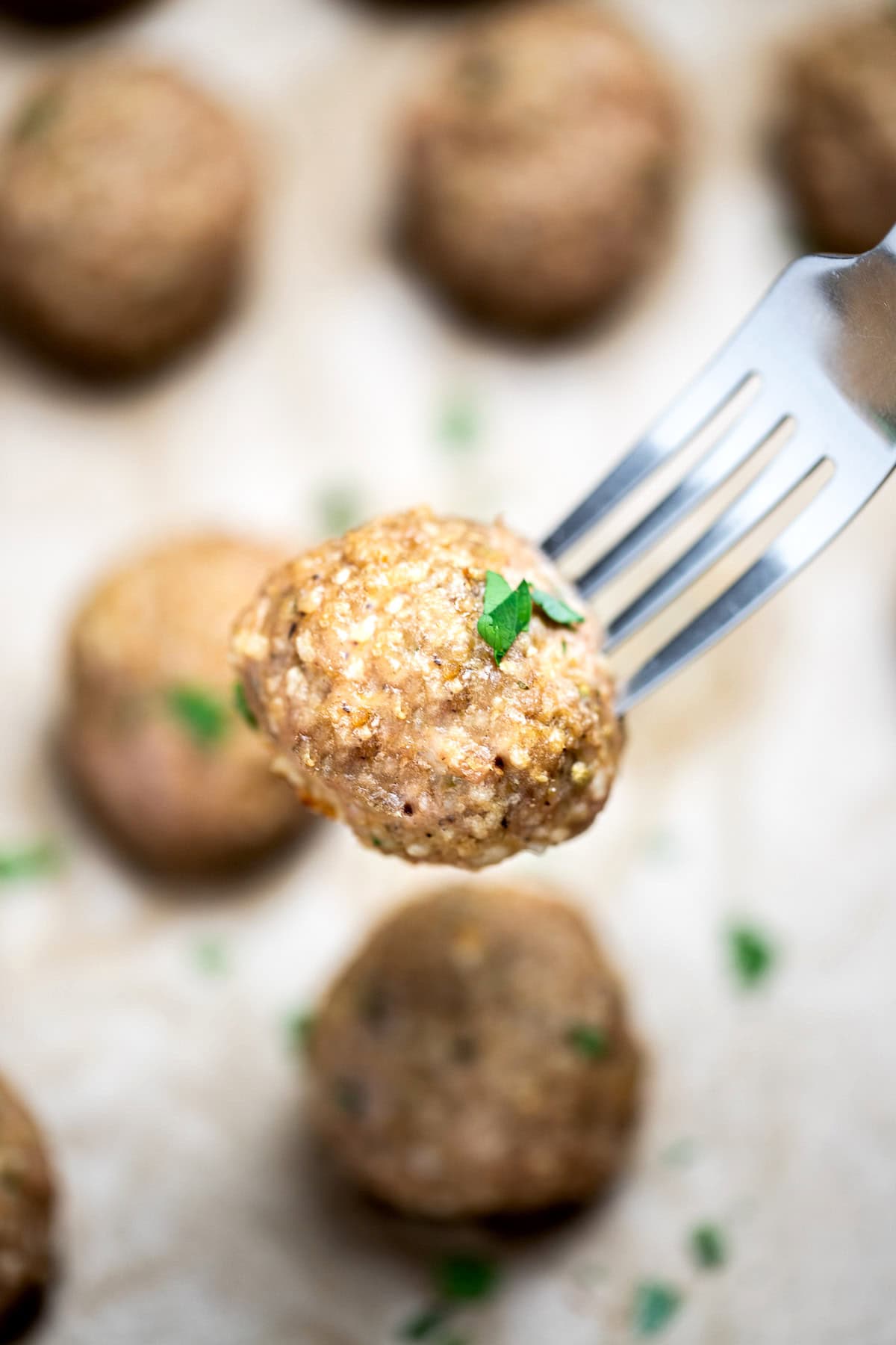 Baked turkey meatballs on a sheet pan lined with parchment paper, fully cooked and topped with fresh chopped parsley, with a fork lifting one meatball up.