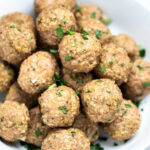 A bowl full of baked turkey meatballs topped with fresh chopped parsley, on a table.