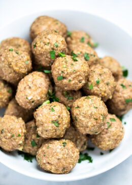 A bowl full of baked turkey meatballs topped with fresh chopped parsley, on a table.