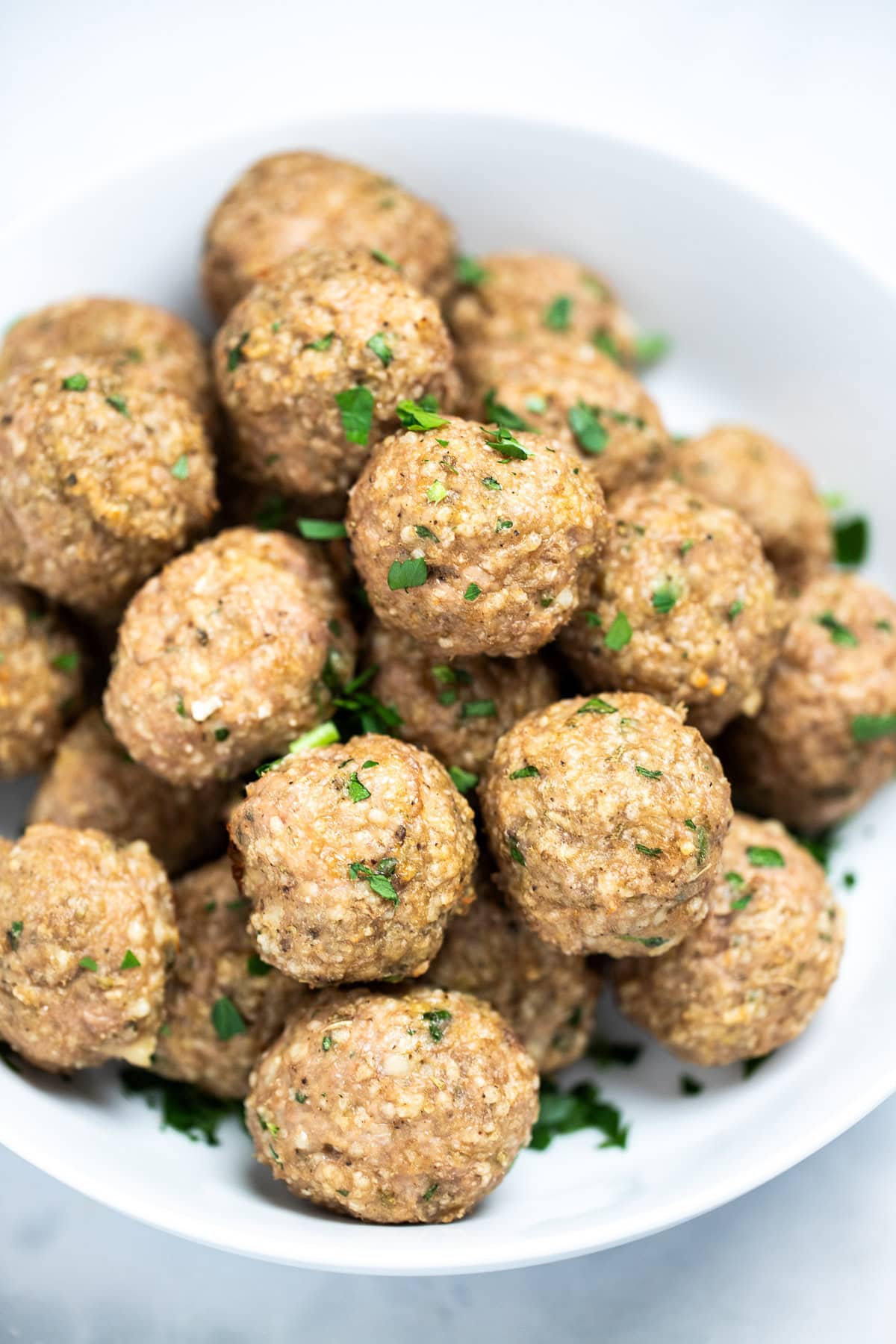 A bowl full of baked turkey meatballs topped with fresh chopped parsley, on a table.