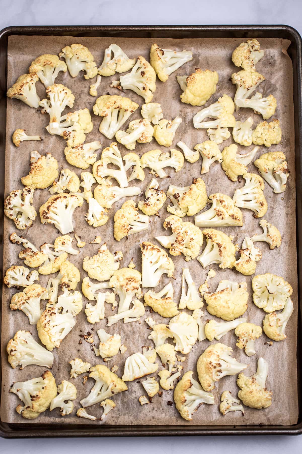 A sheet pan lined with parchment paper with roasted cauliflower florets.