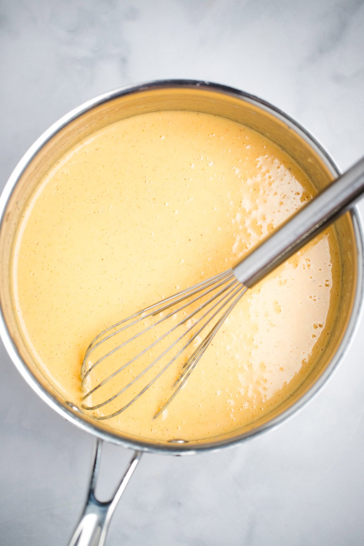 A saucepan full of cheese sauce with a whisk sitting in the sauce.