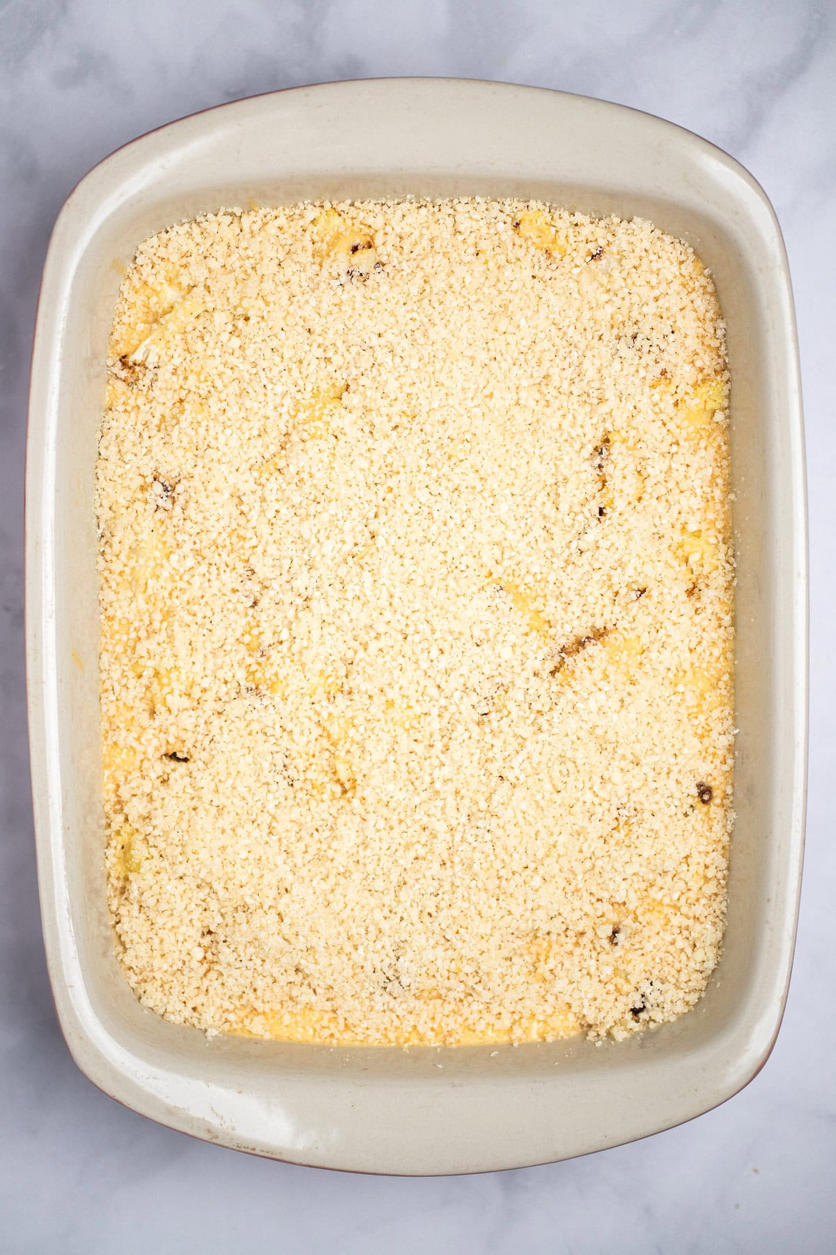 A baking dish full of cauliflower mac and cheese with a breadcrumb topping before being baked.