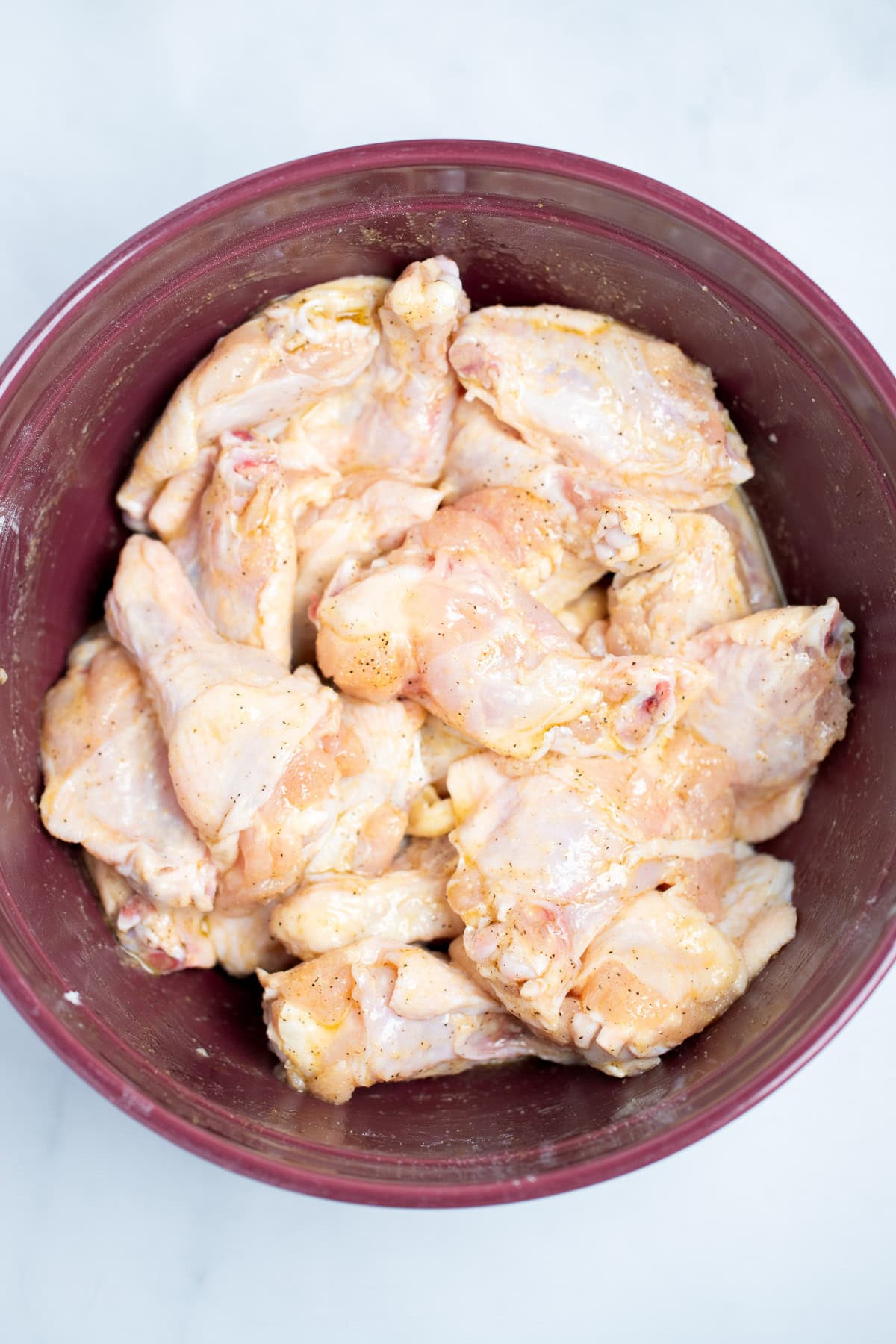 A mixing bowl with raw chicken wings coated with olive oil and spices.