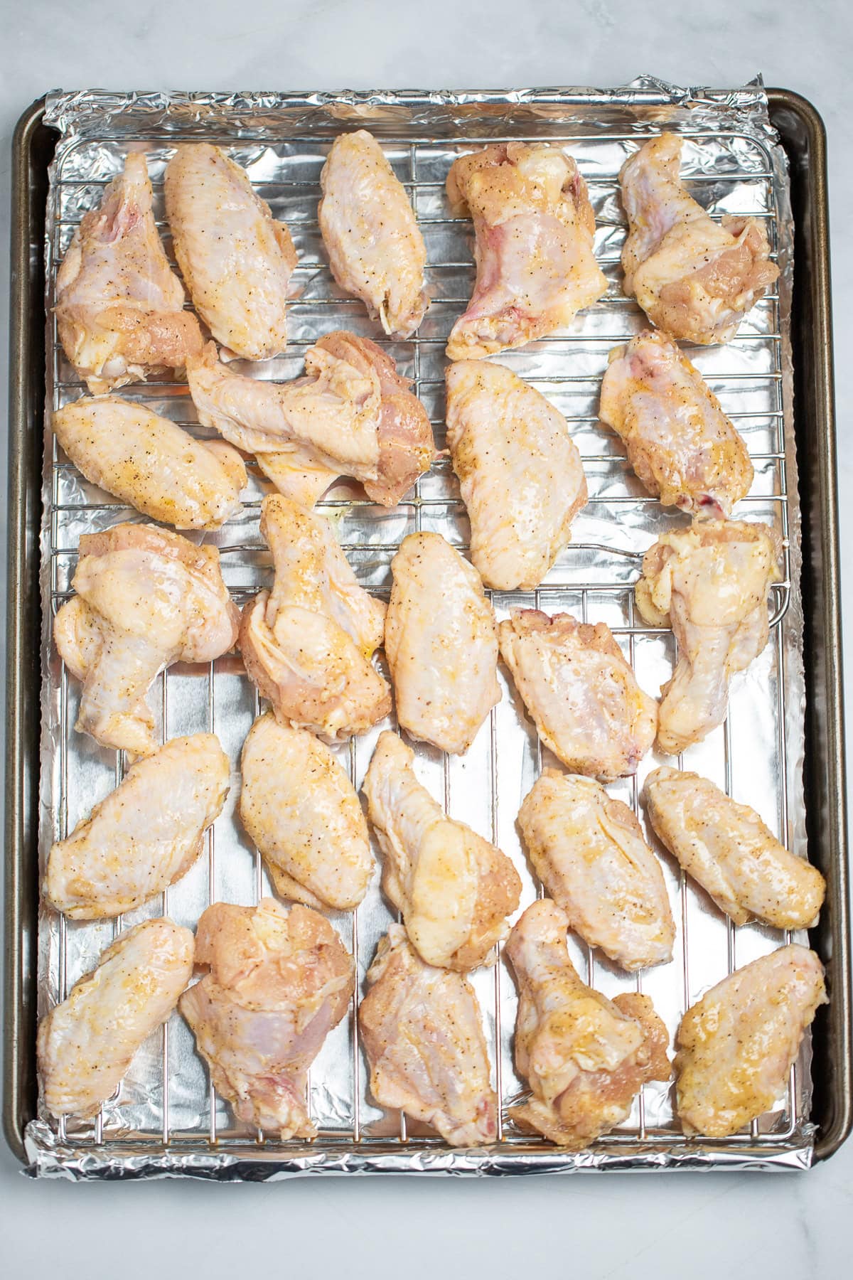 A sheet pan lined with tinfoil and a baking rack with raw seasoned chicken wings on it.