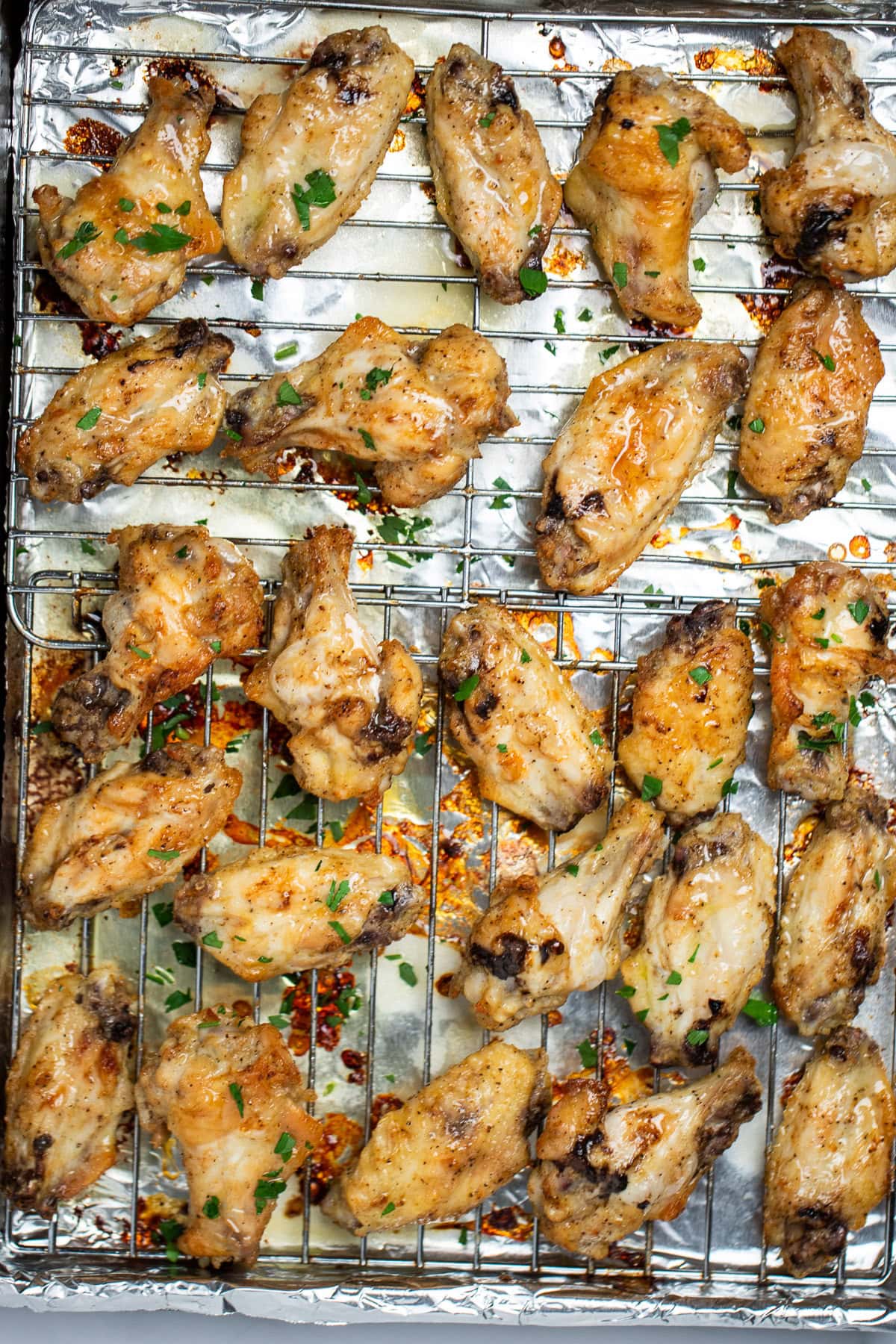 A sheet pan lined with tinfoil and a baking rack with cooked lemon pepper chicken wings topped with fresh parsley.