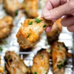 A hand holding a chicken wing above a baking rack of cooked chicken wings topped with fresh parsley.