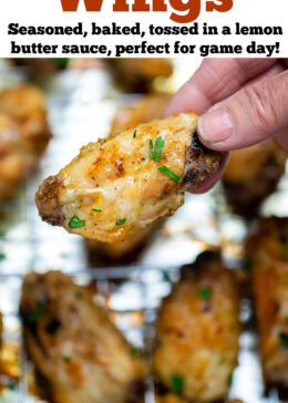 Pinterest pin with a hand holding a chicken wing above a baking rack of cooked chicken wings topped with fresh parsley.